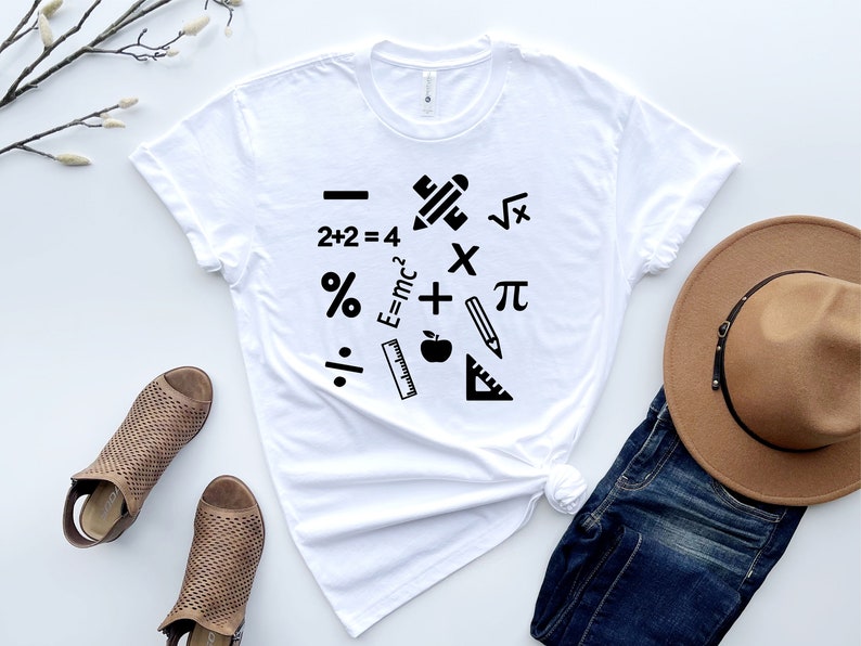 May include: White t-shirt with a black graphic design of math symbols and school supplies, including a pencil, ruler, apple, plus sign, minus sign, multiplication sign, division sign, percentage sign, pi symbol, square root symbol, and the equation E=mc&sup2;.