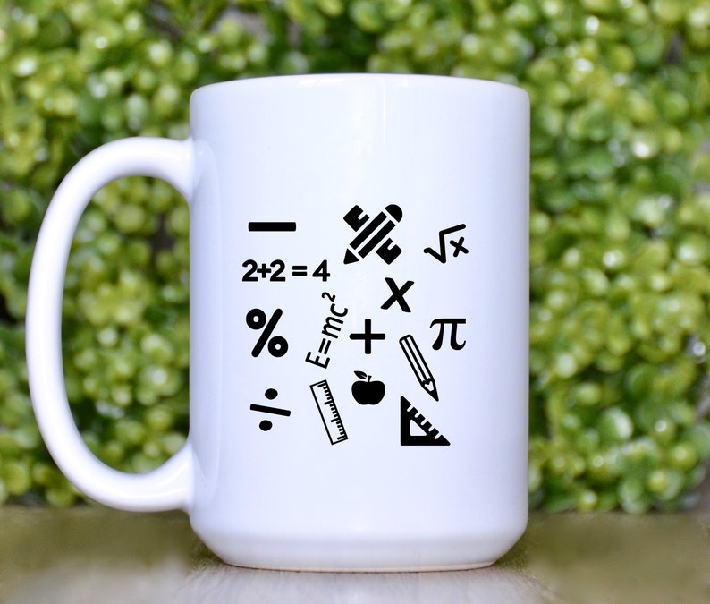 May include: White ceramic coffee mug with black mathematical symbols and icons, including a pencil, ruler, apple, plus sign, percentage sign, division sign, square root symbol, pi symbol, and the equation E=mc2.
