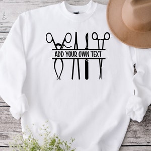 May include: White sweatshirt with a black design of surgical instruments, including scissors, forceps, and a scalpel. The design includes a banner that says "ADD YOUR OWN TEXT".