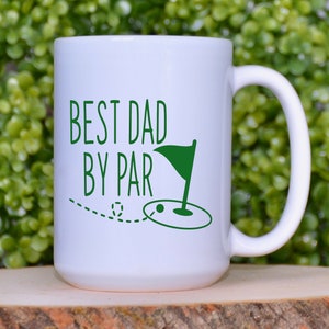 May include: White ceramic coffee mug with a green design that says "Best Dad By Par" with a golf ball and flag.