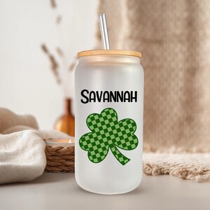 May include: A white tumbler with a green shamrock design and the name "Savannah" printed on it. The tumbler has a bamboo lid and a straw.