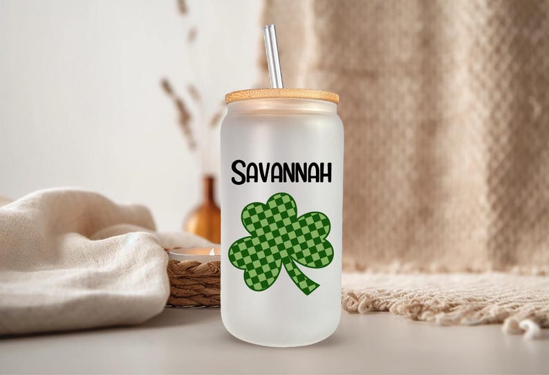May include: A white tumbler with a green shamrock design and the name "Savannah" printed on it. The tumbler has a bamboo lid and a straw.