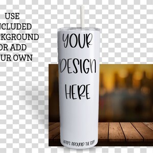 May include: White stainless steel tumbler with a straw. The tumbler has the text "YOUR DESIGN HERE" printed on it. The tumbler is sitting on a wooden surface with a blurred background.