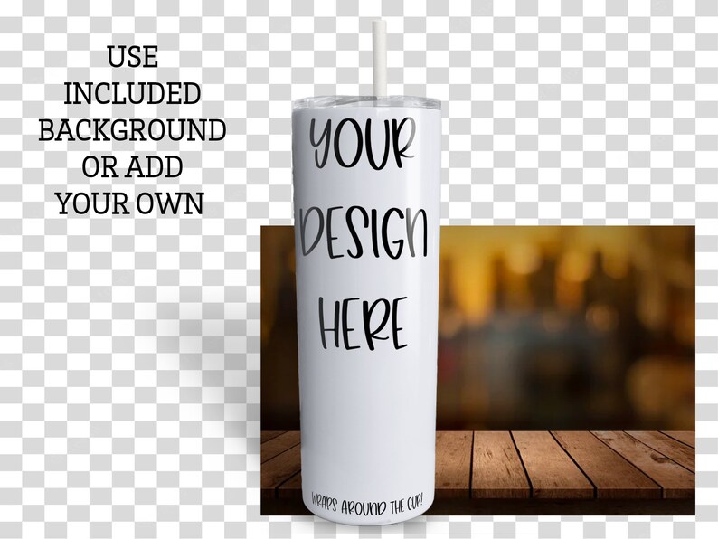 May include: White stainless steel tumbler with a straw. The tumbler has the text "YOUR DESIGN HERE" printed on it. The tumbler is sitting on a wooden surface with a blurred background.