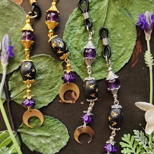 Könnte beinhalten: Drei Paar Brillenketten-Anhänger mit einem Halbmond, einem Stern und violetten Glasperlen. Die Ketten sind golden, silbern und schwarz.