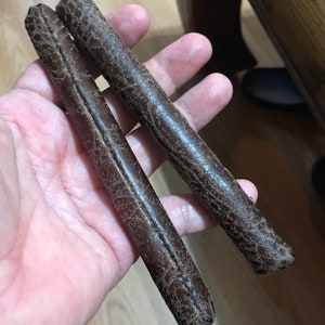 May include: Two brown leather straps with a stitched seam. The straps are about 12 inches long and 1 inch wide.