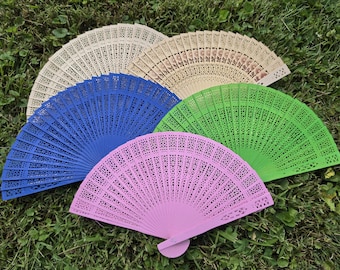 May include: A collection of four folding hand fans arranged in a semi-circle. The fans are made of wood with intricate laser-cut patterns and come in four distinct colors: light beige, vibrant blue, bright green, and a soft pastel pink.