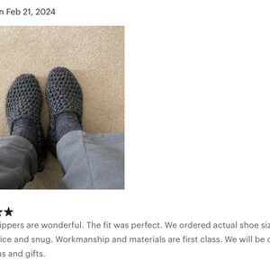 May include: A pair of gray crocheted slippers. The slippers have a textured knit pattern and are worn on a carpeted floor.