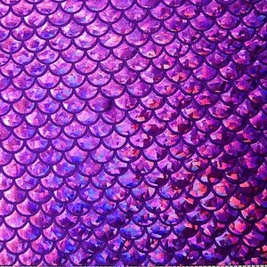 May include: A close-up of a fabric with a mermaid scale pattern. The scales are a gradient of purple and pink, with a shimmering, iridescent effect. The design is a repeating pattern of overlapping, semi-circular shapes.