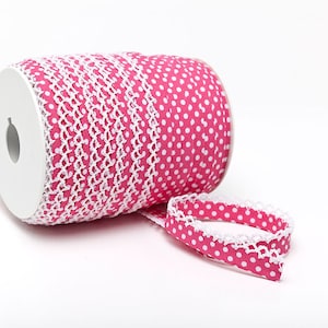 Op de afbeelding: Een rol roze lint met witte stippen en witte kant. Het lint is opgerold op een witte rol.