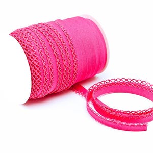 Può includere: Un rotolo di nastro rosa acceso con un delicato bordo traforato. Il nastro è parzialmente srotolato, rivelando una lunghezza dello stesso colore e design. Lo sfondo è bianco.