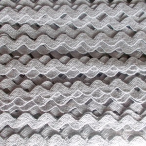 Op de afbeelding: Een close-up van een grijze, gegolfde trim. De trim is gemaakt van een zachte, textuurrijke stof en heeft een licht verhoogd patroon.