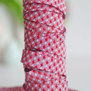Könnte beinhalten: Eine Rolle rotes und weißes Gingham-Band. Das Band ist fest gewickelt und bereit für Bastelarbeiten oder Dekorationen.