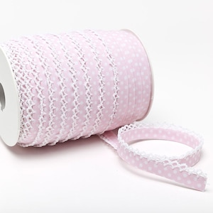 Op de afbeelding: Een spoel met roze elastische trim met witte stippen en een witte gehaakte rand.