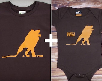May include: A brown t-shirt with a silhouette of a lion and a cub, with the word "PRIDE" printed below. Next to it is a brown baby onesie with a similar lion and cub silhouette and the text "DADDY'S PRIDE".