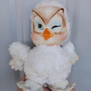 Puede incluir: Juguete vintage de b&uacute;ho de peluche blanco con un gui&ntilde;o. El b&uacute;ho tiene una cabeza color crema con detalles marrones y azules, un pico naranja y mejillas rosadas. El cuerpo est&aacute; cubierto de material de felpa blanco y suave.