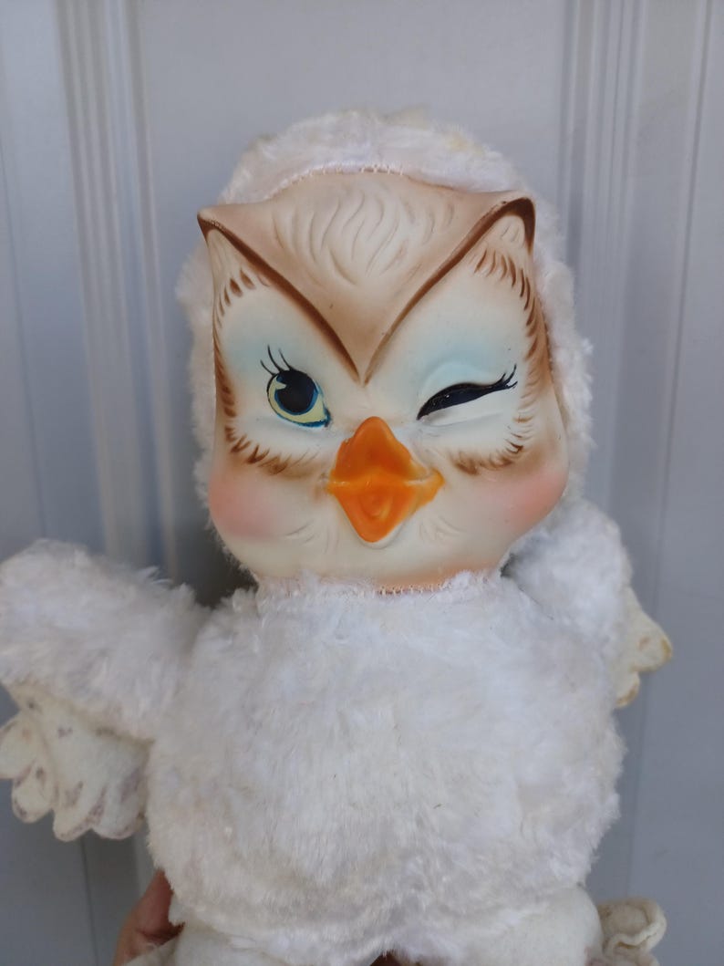 Puede incluir: Una mu&ntilde;eca de b&uacute;ho vintage con una expresi&oacute;n gui&ntilde;ando un ojo. El b&uacute;ho tiene una cara color crema con detalles en marr&oacute;n y azul, un pico naranja y mejillas rosadas. Su cuerpo est&aacute; cubierto de material blanco y esponjoso, y tiene peque&ntilde;as alas extendidas.