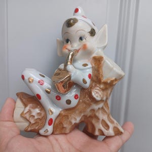 Kitsch vintage anni &#39;50, elfo musicista folletto che suona il sassofono su un tronco, uccello mancante così com&#39;è