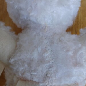 Puede incluir: Primer plano de la espalda de un peluche blanco. El juguete de peluche tiene un aspecto esponjoso y texturizado. Las costuras visibles recorren el centro de la espalda y el cuerpo del juguete est&aacute; hecho de un material blanco y suave.