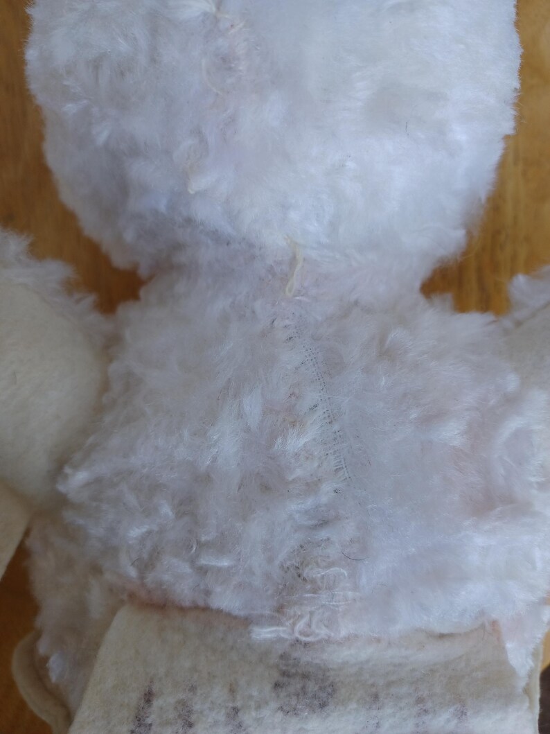 Puede incluir: Primer plano de la espalda de un peluche blanco. El juguete de peluche tiene un aspecto esponjoso y texturizado. Las costuras visibles recorren el centro de la espalda y el cuerpo del juguete est&aacute; hecho de un material blanco y suave.