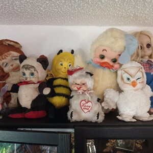 Puede incluir: Una colecci&oacute;n de juguetes de peluche vintage, que incluyen un panda, una abeja, un pato y un b&uacute;ho. Los juguetes est&aacute;n colocados en un estante, mostrando sus diversos colores y dise&ntilde;os. Algunos juguetes tienen etiquetas en forma de coraz&oacute;n con la inscripci&oacute;n "Love me".
