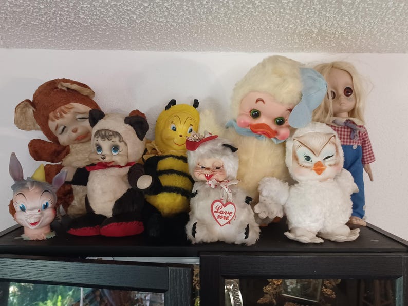 Puede incluir: Una colecci&oacute;n de juguetes de peluche vintage, que incluyen un panda, una abeja, un pato y un b&uacute;ho. Los juguetes est&aacute;n colocados en un estante, mostrando sus diversos colores y dise&ntilde;os. Algunos juguetes tienen etiquetas en forma de coraz&oacute;n con la inscripci&oacute;n "Love me".