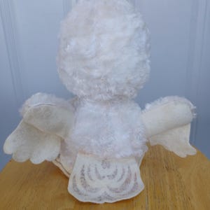 Puede incluir: Un juguete de p&aacute;jaro de peluche blanco vintage con un cuerpo esponjoso, alas de fieltro y una cola decorativa. El p&aacute;jaro est&aacute; posicionado sobre una superficie de madera, mostrando su espalda y alas. La textura suave y el dise&ntilde;o del juguete sugieren que es un art&iacute;culo de colecci&oacute;n.