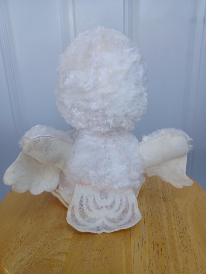 Puede incluir: Un juguete de p&aacute;jaro de peluche blanco vintage con un cuerpo esponjoso, alas de fieltro y una cola decorativa. El p&aacute;jaro est&aacute; posicionado sobre una superficie de madera, mostrando su espalda y alas. La textura suave y el dise&ntilde;o del juguete sugieren que es un art&iacute;culo de colecci&oacute;n.