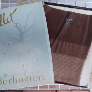 May include: An open box of vintage hosiery. The box is light blue with gold lettering that reads "Ballet by Burlington." Inside, sheer brown stockings are visible, along with tissue paper. The stockings have a diamond pattern near the foot.