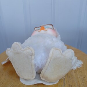 Puede incluir: Un juguete de peluche de b&uacute;ho blanco vintage con grandes pies de fieltro. El b&uacute;ho tiene un pico de color naranja claro, ojos azules y un cuerpo suave y esponjoso. El b&uacute;ho est&aacute; acostado sobre su espalda sobre una superficie de madera.