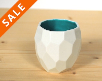 May include: White ceramic cup with a geometric design and a teal blue interior.