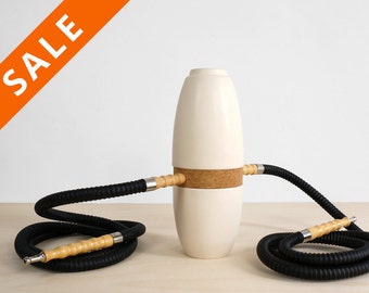 May include: White ceramic hookah with two black hoses and wooden mouthpieces. The hookah has a cork band around the middle.