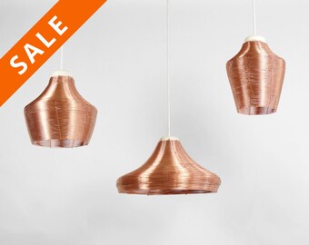 May include: Three copper wire pendant lights hanging from white cords against a white background.