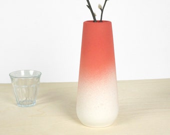 May include: A red and white ombre ceramic vase with a narrow opening and a wide base. The vase is sitting on a light wood surface.