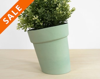 May include: A tilted, light green plant pot filled with a green and white leafy plant. The pot has a classic shape with a wide rim. An orange diagonal banner with the word "SALE" is in the upper left corner.