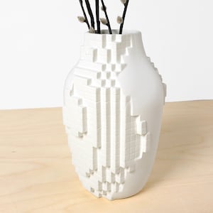 Könnte beinhalten: Weiße Keramikvase mit geometrischem, pixeligem Design. Die Vase hat die Form einer traditionellen Vase mit einem runden Körper und einem schmalen Hals.