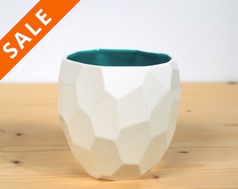 May include: White ceramic planter with a teal blue interior. The planter has a geometric, faceted design.