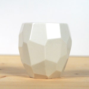 May include: A white ceramic planter with a geometric, faceted design. The planter has a rounded shape and a smooth, glossy finish.