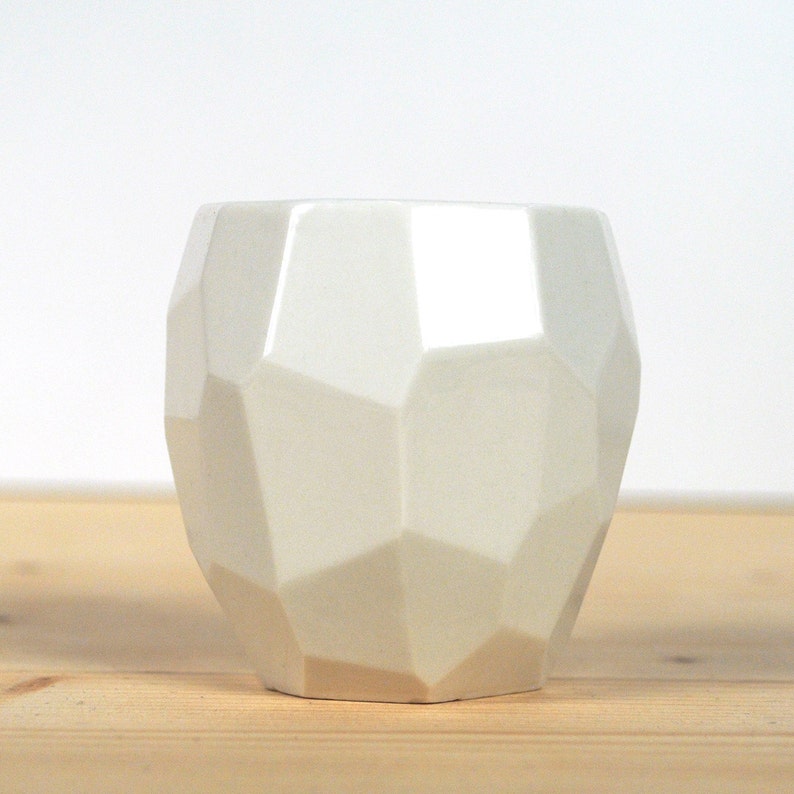 May include: A white ceramic planter with a geometric, faceted design. The planter has a rounded shape and a smooth, glossy finish.
