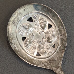 May include: A silver serving spoon with a decorative, openwork design in the bowl. The spoon has a long, slender handle.