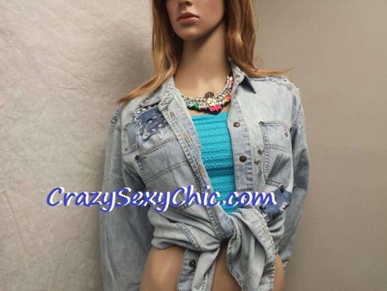 May include: A light blue denim jacket with distressed details and a turquoise tank top underneath. The jacket is tied at the waist and features a colourful beaded necklace.