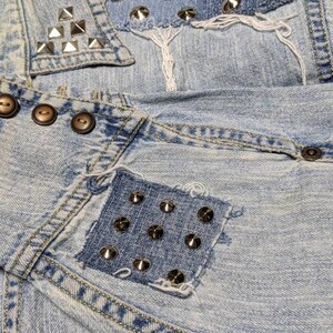 May include: Light blue denim jacket with multiple patches and silver studs. The patches are made of denim and have frayed edges. The jacket has a collar and a button closure.