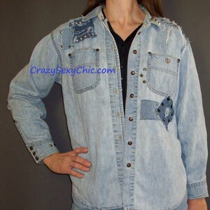 May include: Light blue denim shirt with a patchwork design and silver studs. The shirt has a button-up front and long sleeves. The shirt is distressed and has a vintage look.