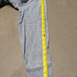 May include: Light blue denim jacket with a frayed hem and a yellow measuring tape showing the length of the sleeve is 50.8 cm.