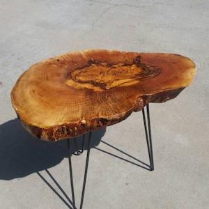 May include: A wooden coffee table with a natural wood finish and a live edge top. The table has black hairpin legs.