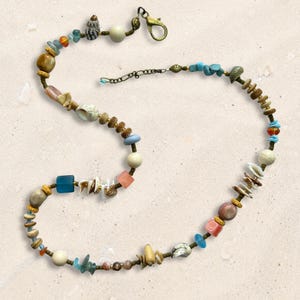 May include: A beaded necklace featuring a variety of natural elements including small seashells, smooth round beads in cream and brown, translucent blue and pink glass cubes, and turquoise stone chips, finished with a brass lobster claw clasp.