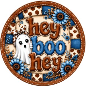 May include: A circular sign featuring a white ghost wearing a brown and white patterned headband. The text "hey boo hey" is displayed in brown and blue letters. The background consists of a blue and cream patchwork quilt pattern with blue sunflowers.