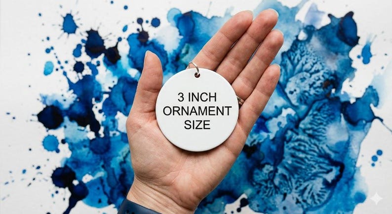 Puede incluir: Un adorno circular de cer&aacute;mica blanca con el texto negro 3 INCH ORNAMENT SIZE impreso en el centro. El adorno incluye una peque&ntilde;a anilla de metal plateado en la parte superior para colgarlo, proporcionando una referencia visual clara de las medidas.