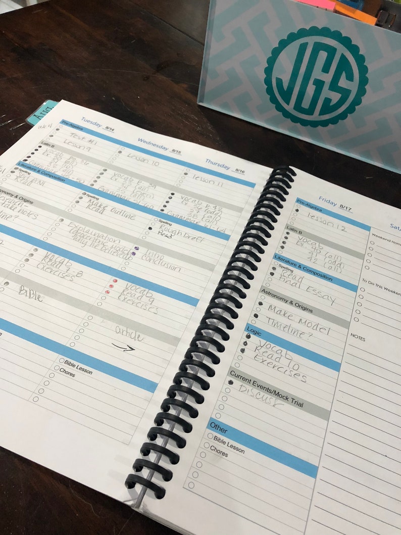 May include: A weekly planner with a black spiral binding. The planner has a blue and white cover with the days of the week listed across the top. The planner is open to Friday, August 17th, and the page has a list of tasks for the day, including "vocab read exercises", "final essay", and "make model timeline".