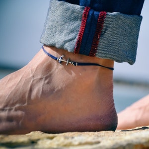 Puede incluir: Un tobillo con un tobillo de cuerda azul con un dije de ancla de plata.